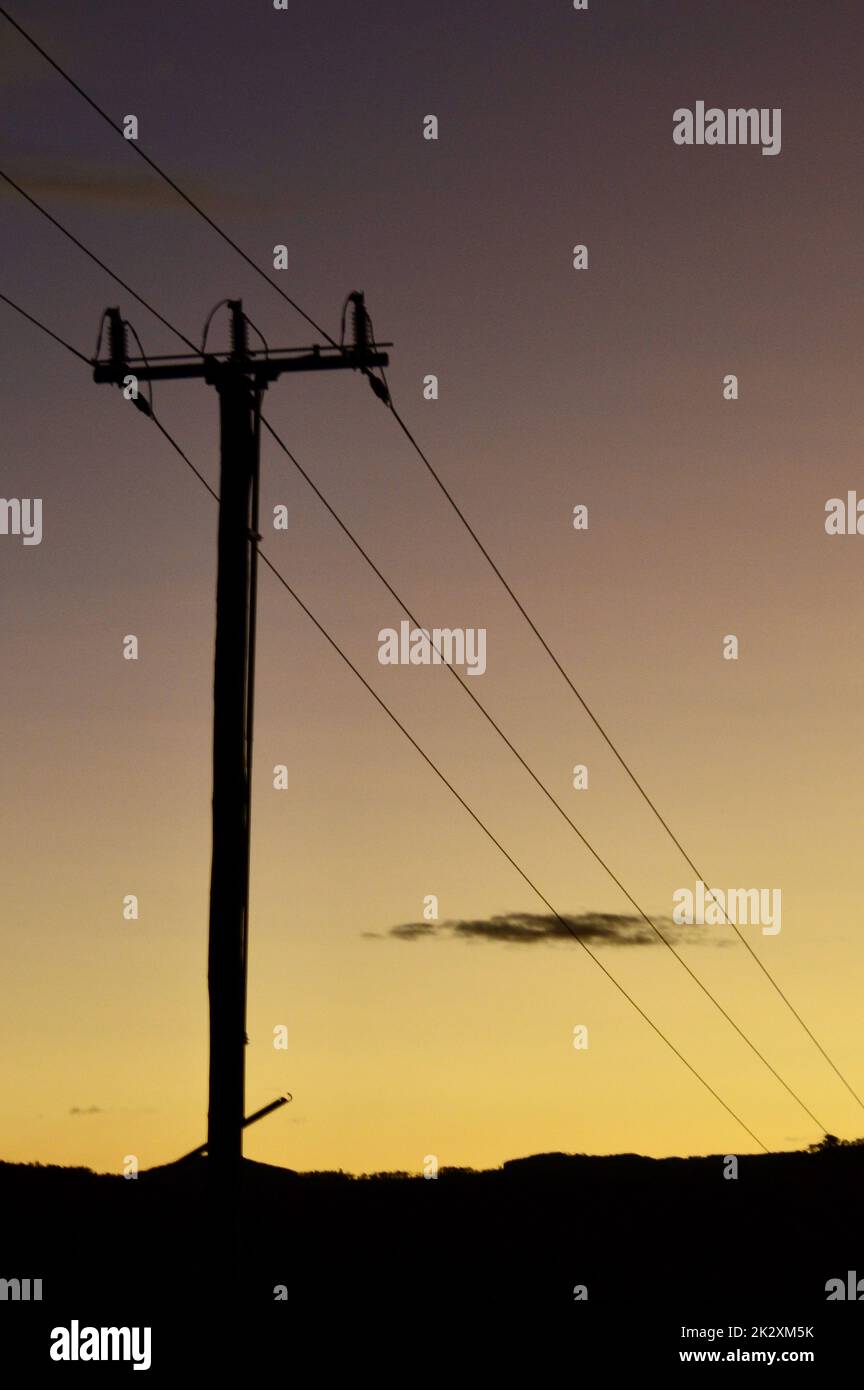 Power poles by a country road at sunset Stock Photo