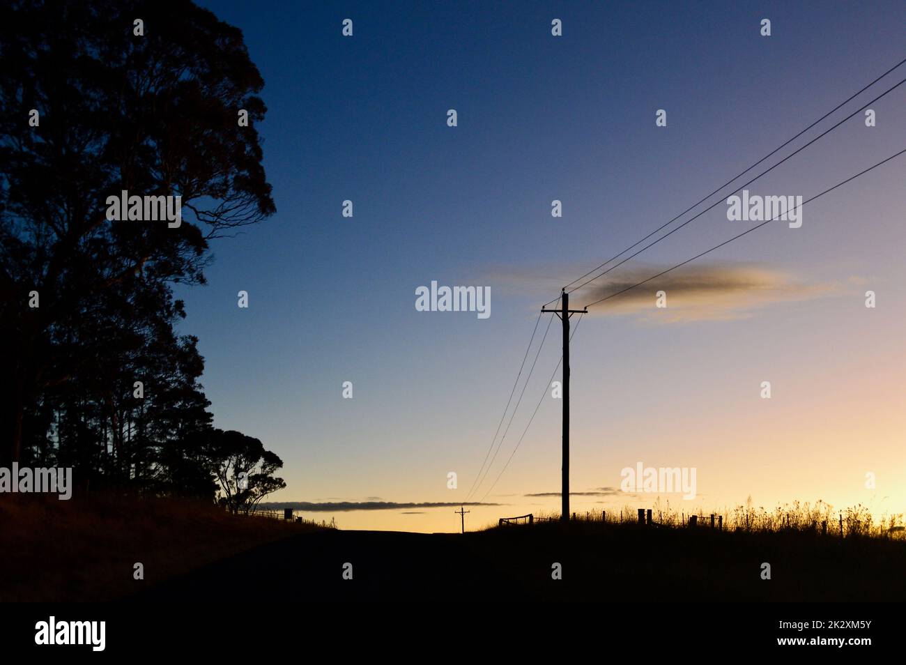 Power poles by a country road at sunset Stock Photo