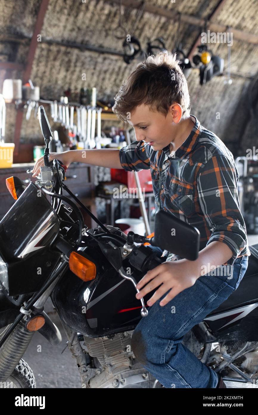 Boy pretending to ride motorcycle in barn Stock Photo