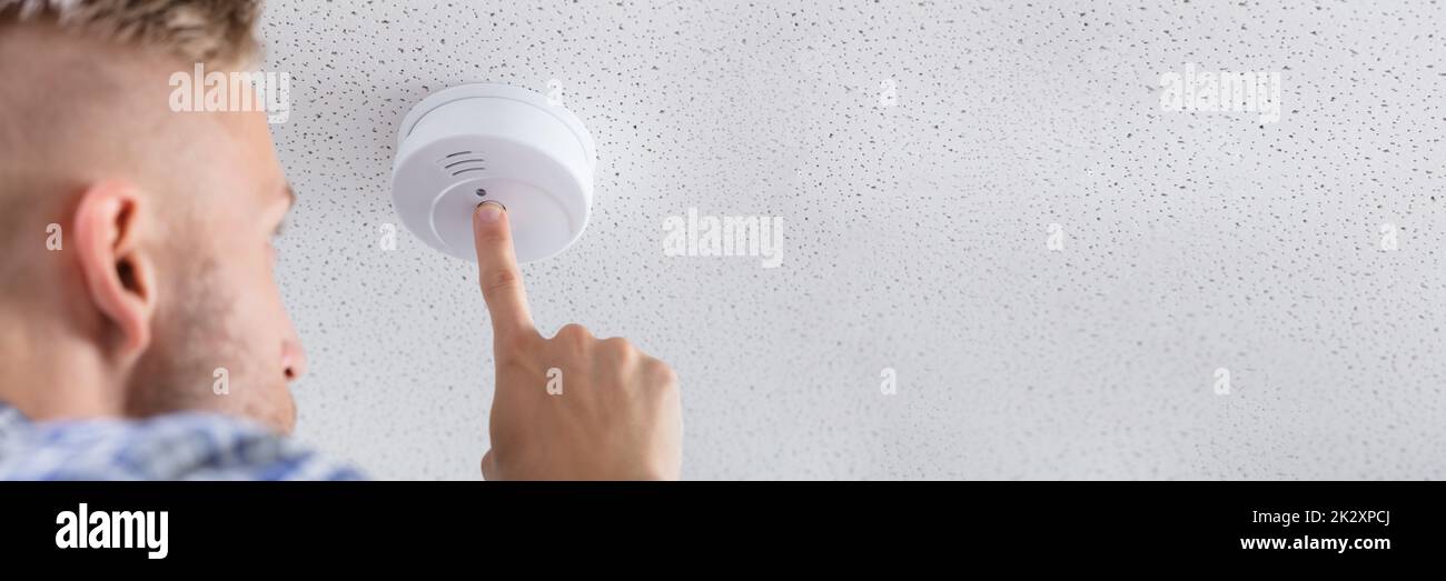 Person's Hand Installing Smoke Detector On Ceiling Stock Photo