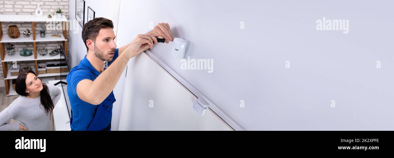 Electrician Installing Security System Motion Detector On Wall Stock Photo