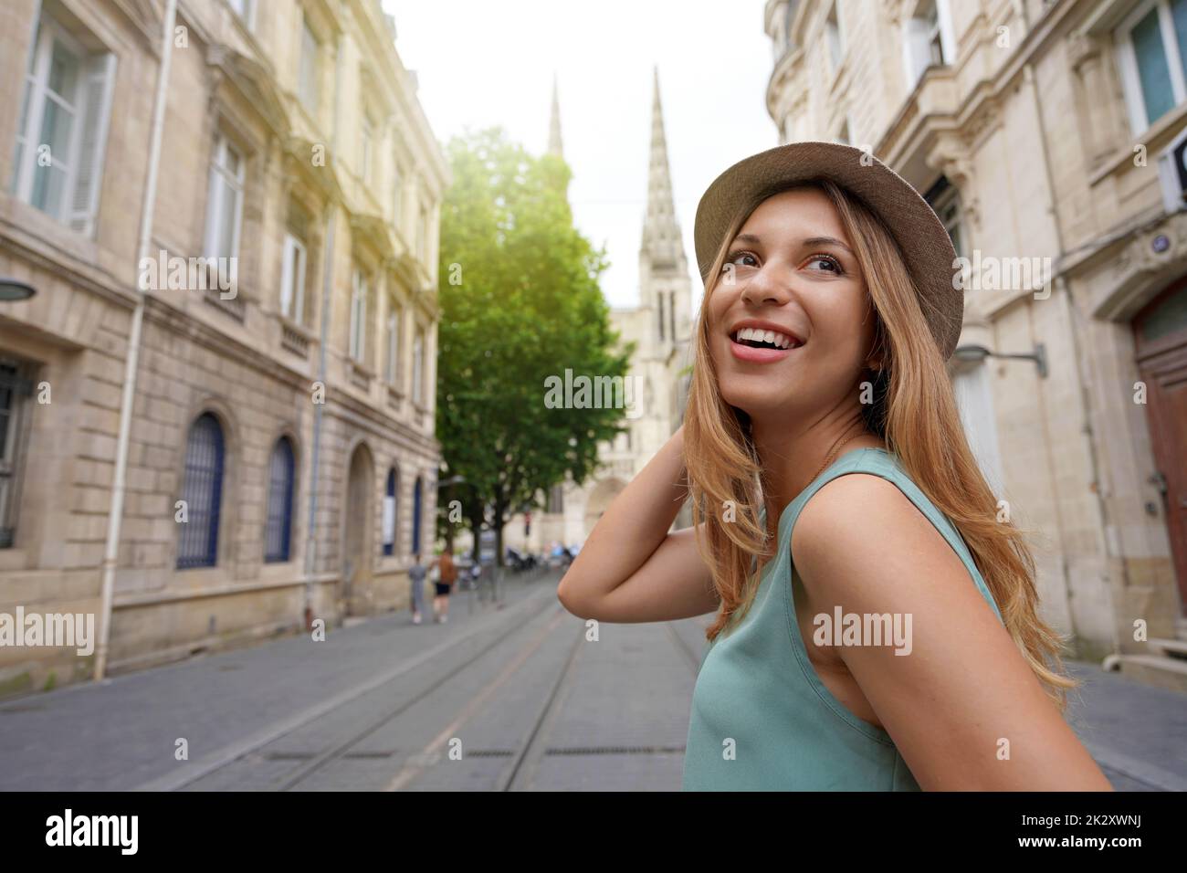 Stylish traveler girl turns around when walking in Bordeaux street with the cathedral on the background, France Stock Photo