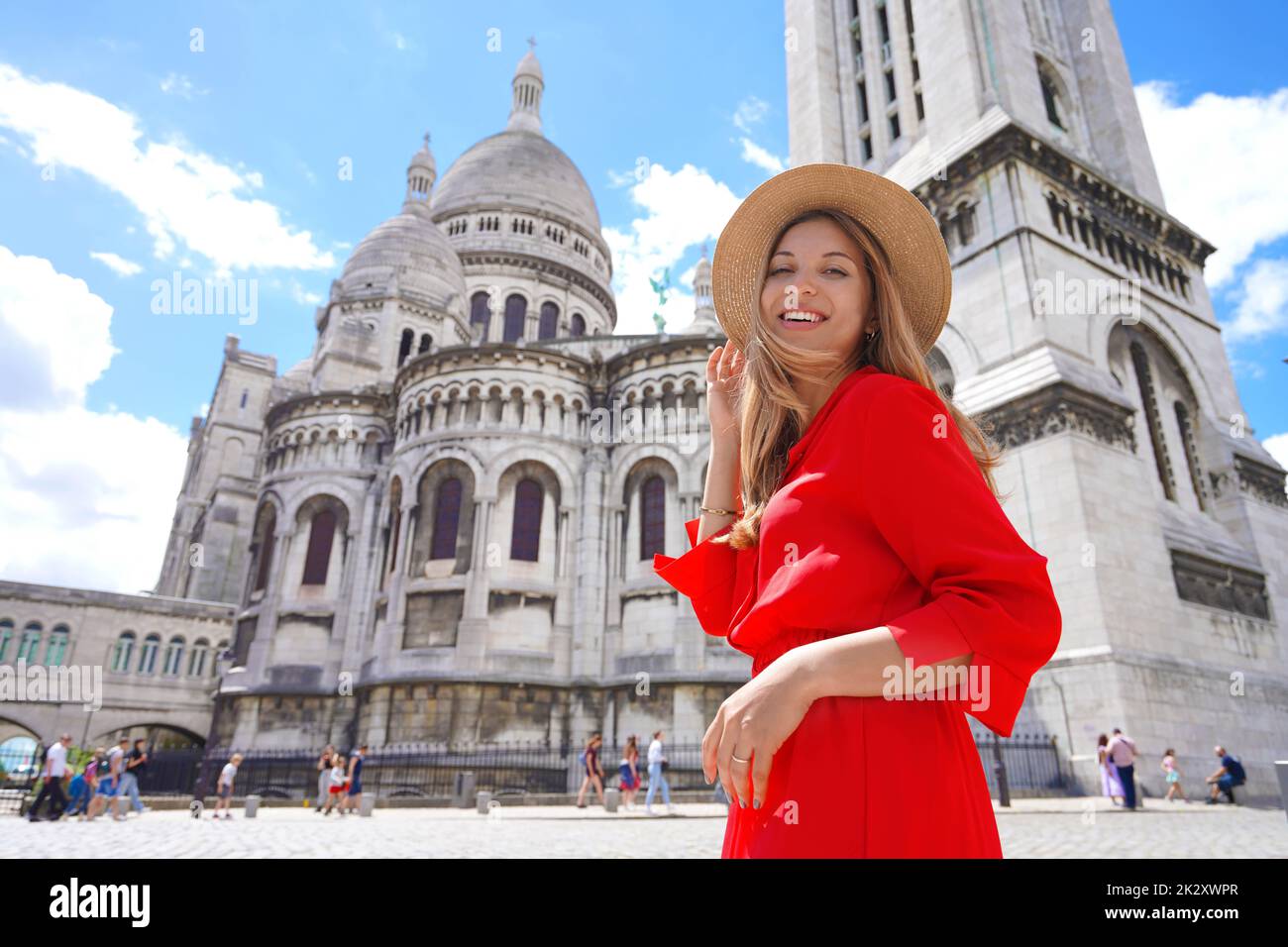 Fashion model walking in Paris with the Basilica of the Sacred Heart of Paris on the background. Smiling at camera. Low angle. Stock Photo