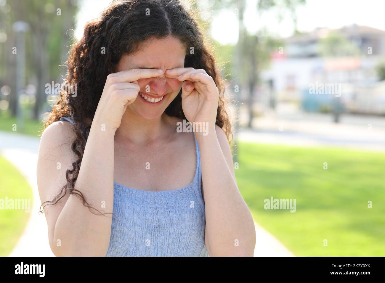 Stressed woman scratching itchy eyes while walks in a park Stock Photo