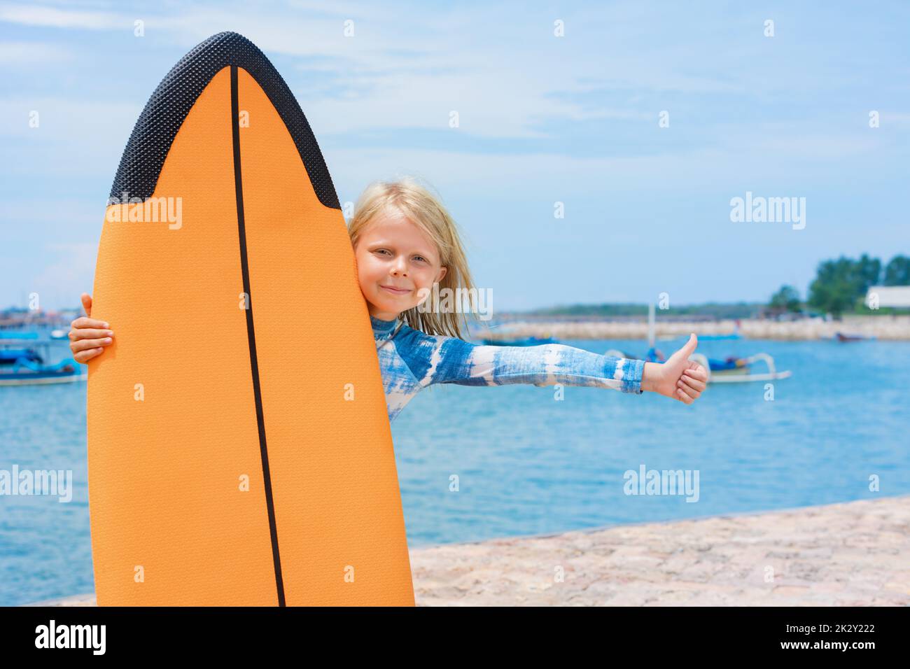 Happy baby girl - young surfer learn to ride on surfboard with fun on sea waves. Active family lifestyle, kids outdoor water sport lessons, surfing Stock Photo