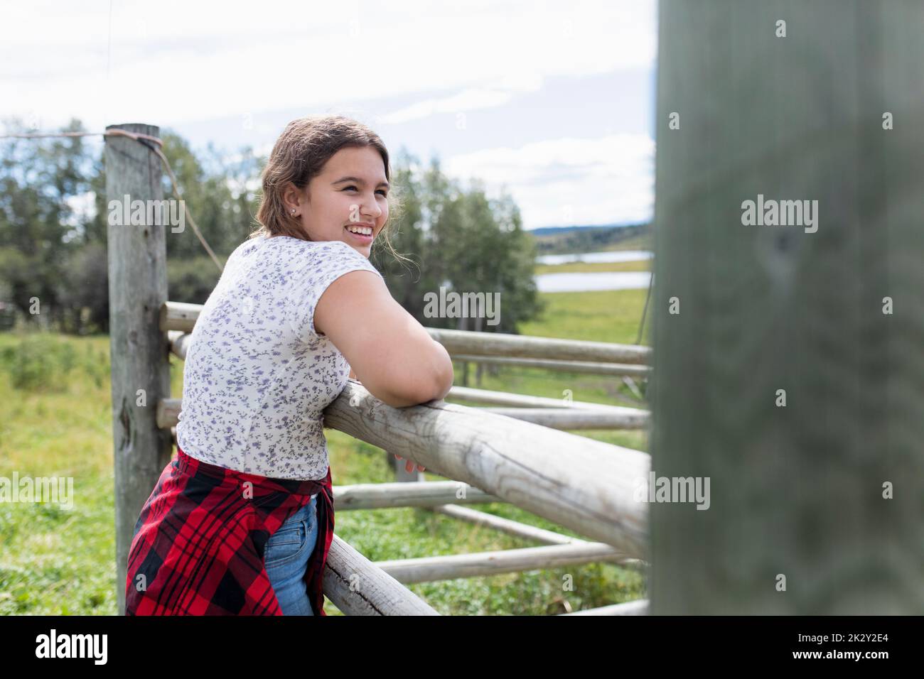 Happy preteen girl at pasture fence on sunny farm Stock Photo