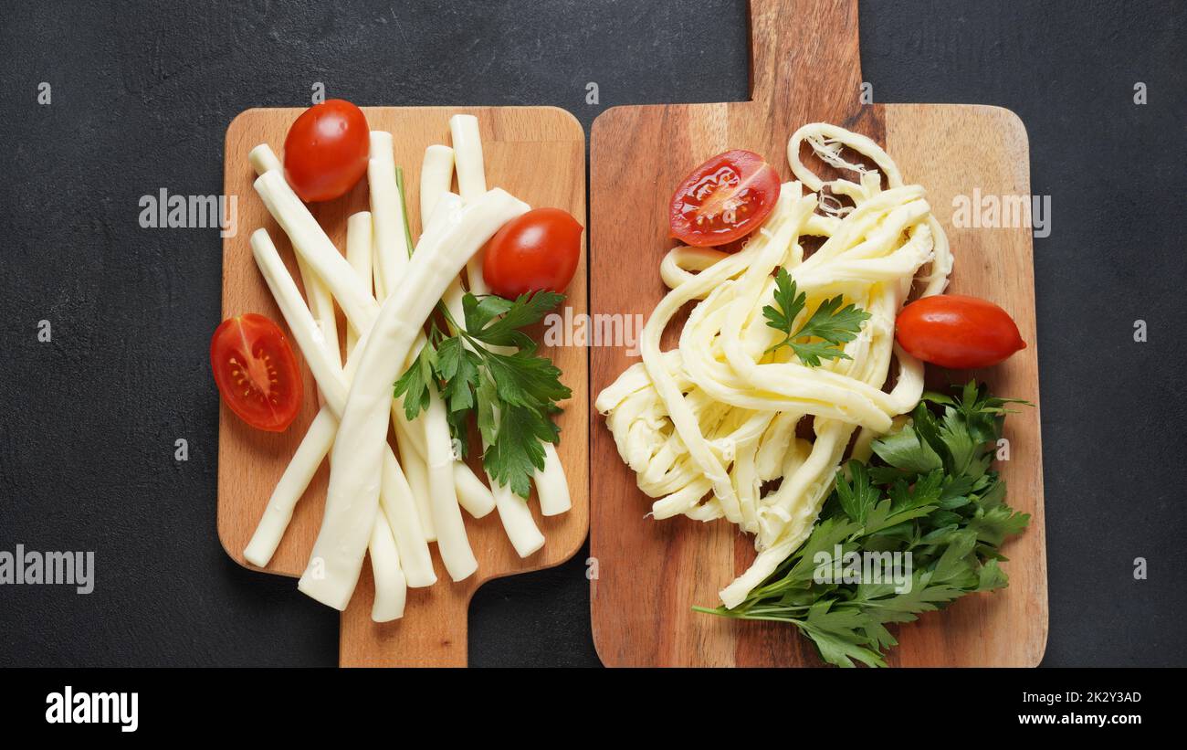 String cheese or cheese whip - salty snack cheese with cherry tomatoes and herbs on chopping board. Turkish cheese Stock Photo