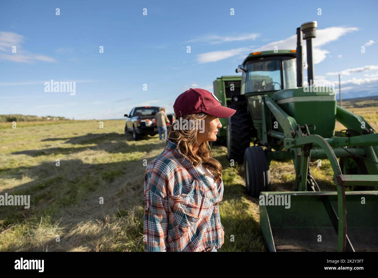Female farmer in baseball cap outside tractor in sunny farm field Stock