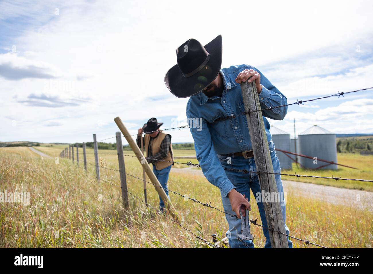 Male ranchers in cowboy hats fixing barbed wire fence on sunny ranch