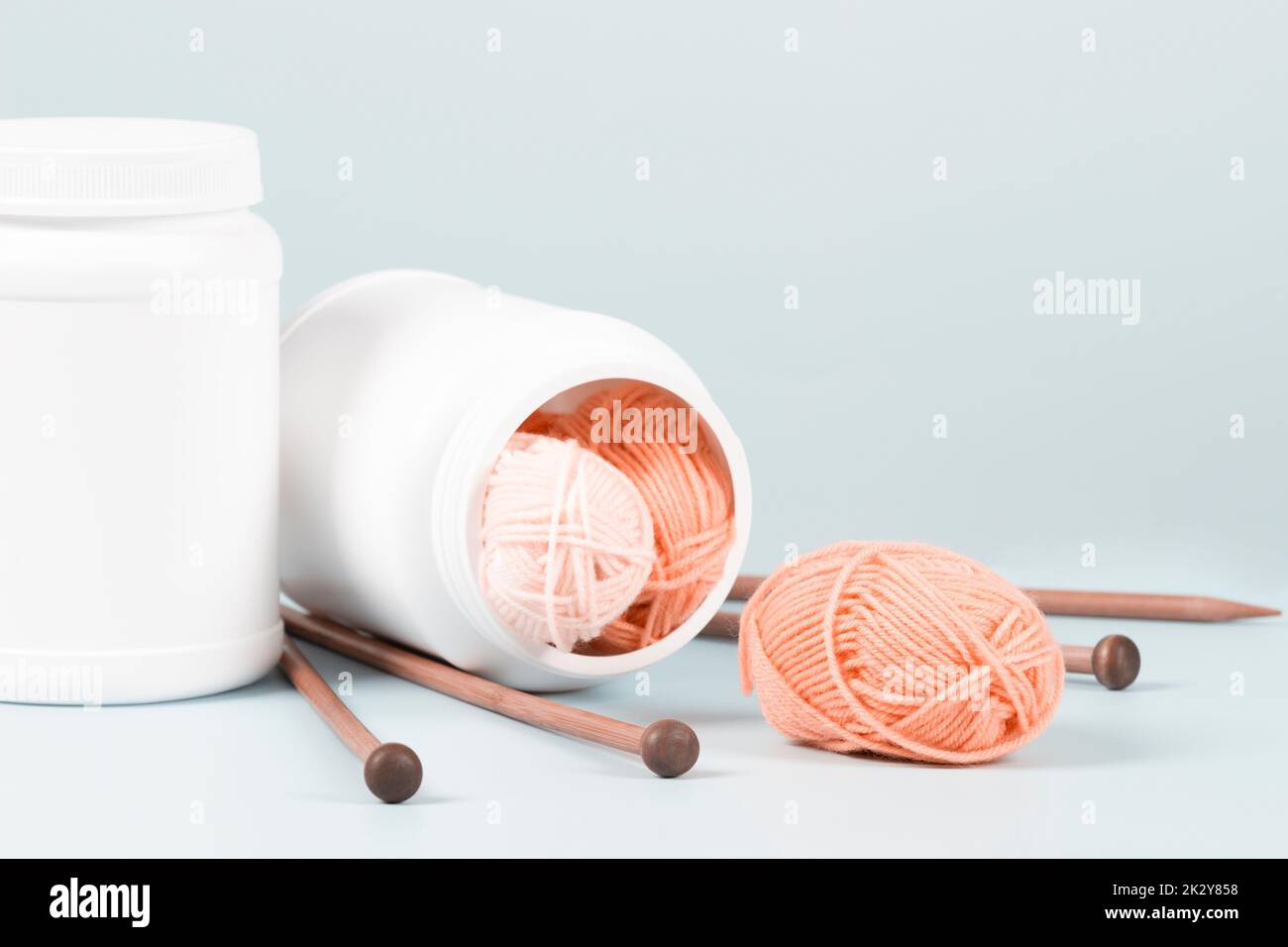 Knitting as therapy. Supplement bottle with balls of yarn and knitting needles on a light blue background. Knitting health benefits, stress reduction Stock Photo
