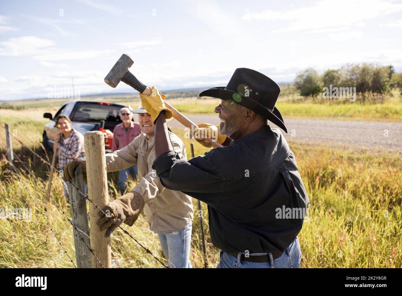 Happy senior male rancher pounding fence post with sledgehammer Stock Photo