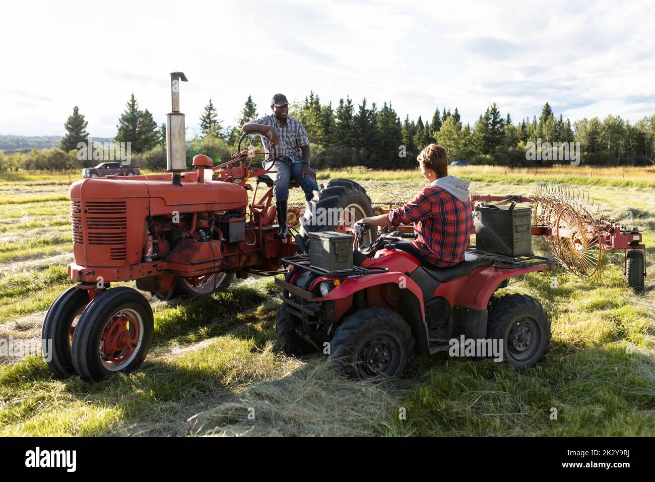 Male farmers talking on tractors in sunny rural field Stock Photo Alamy