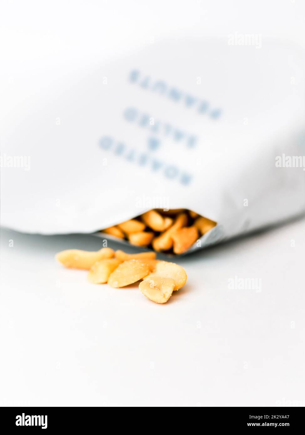 Salted peanuts spilling out of a packet.   Isolated against white background. Stock Photo