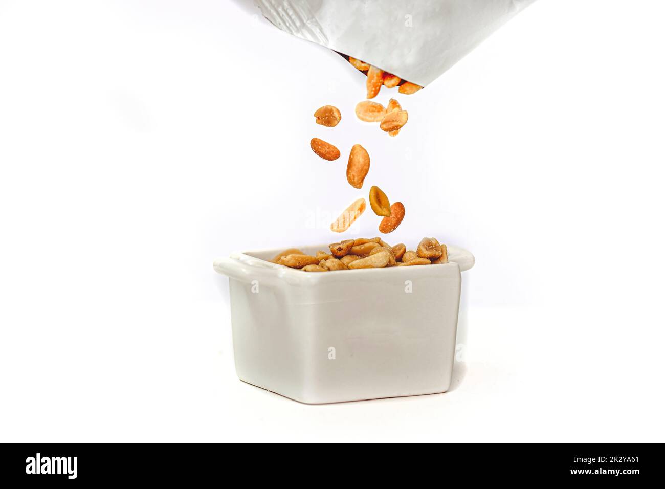 Salted peanuts falling out of a packet into a pot full of peanuts.  Isolated against white background Stock Photo
