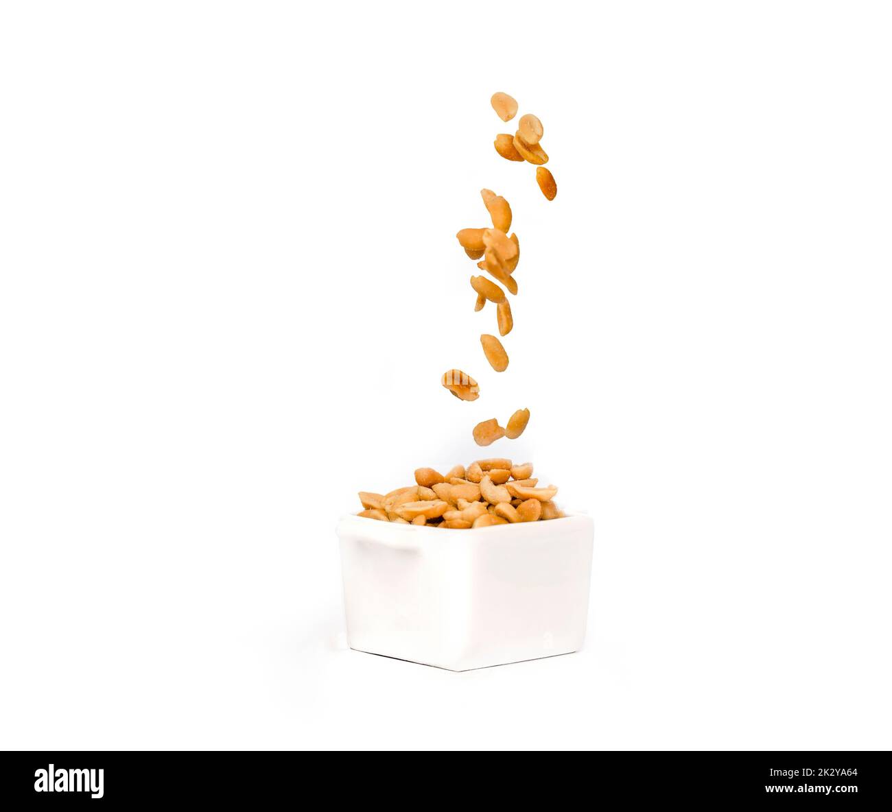 Salted peanuts falling o into a pot full of peanuts.  Isolated against white background Stock Photo