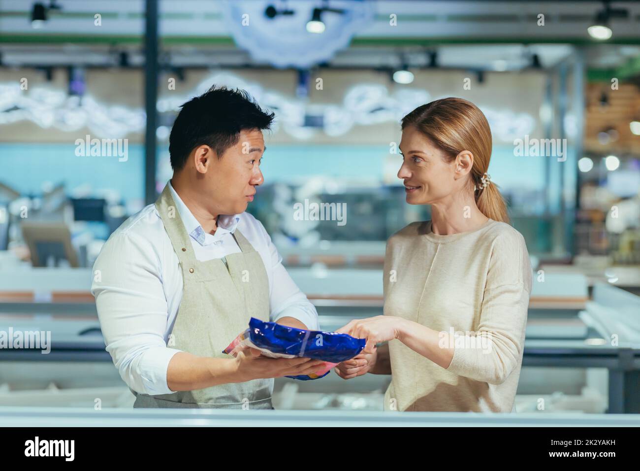 a male consultant in a grocery store advises a woman talking to assistant. seller at vegetable market help customer in supermarket female food girl shop product man choice Asian guy consultor help. Stock Photo