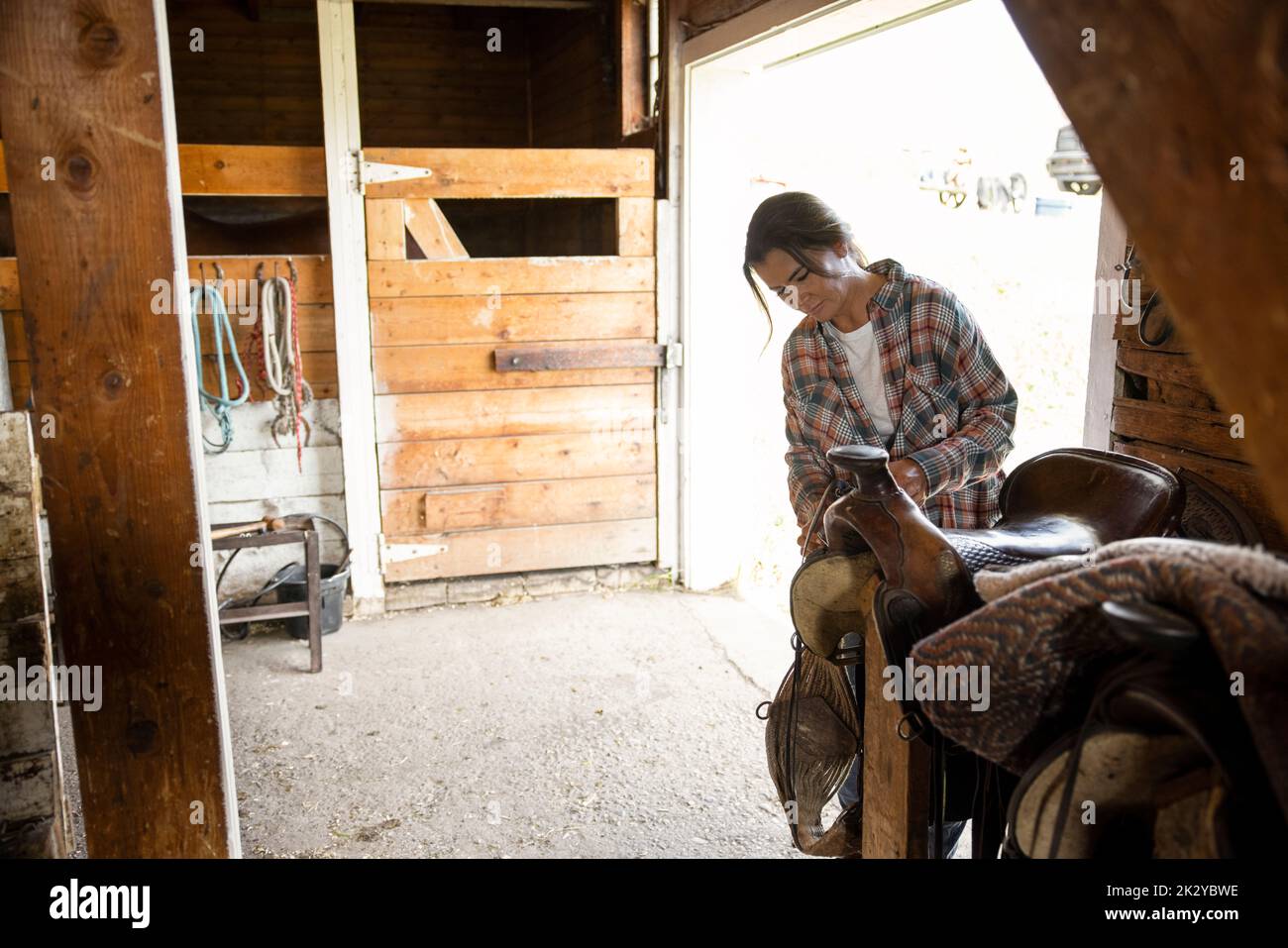 Female rancher cleaning saddle in horse barn Stock Photo Alamy
