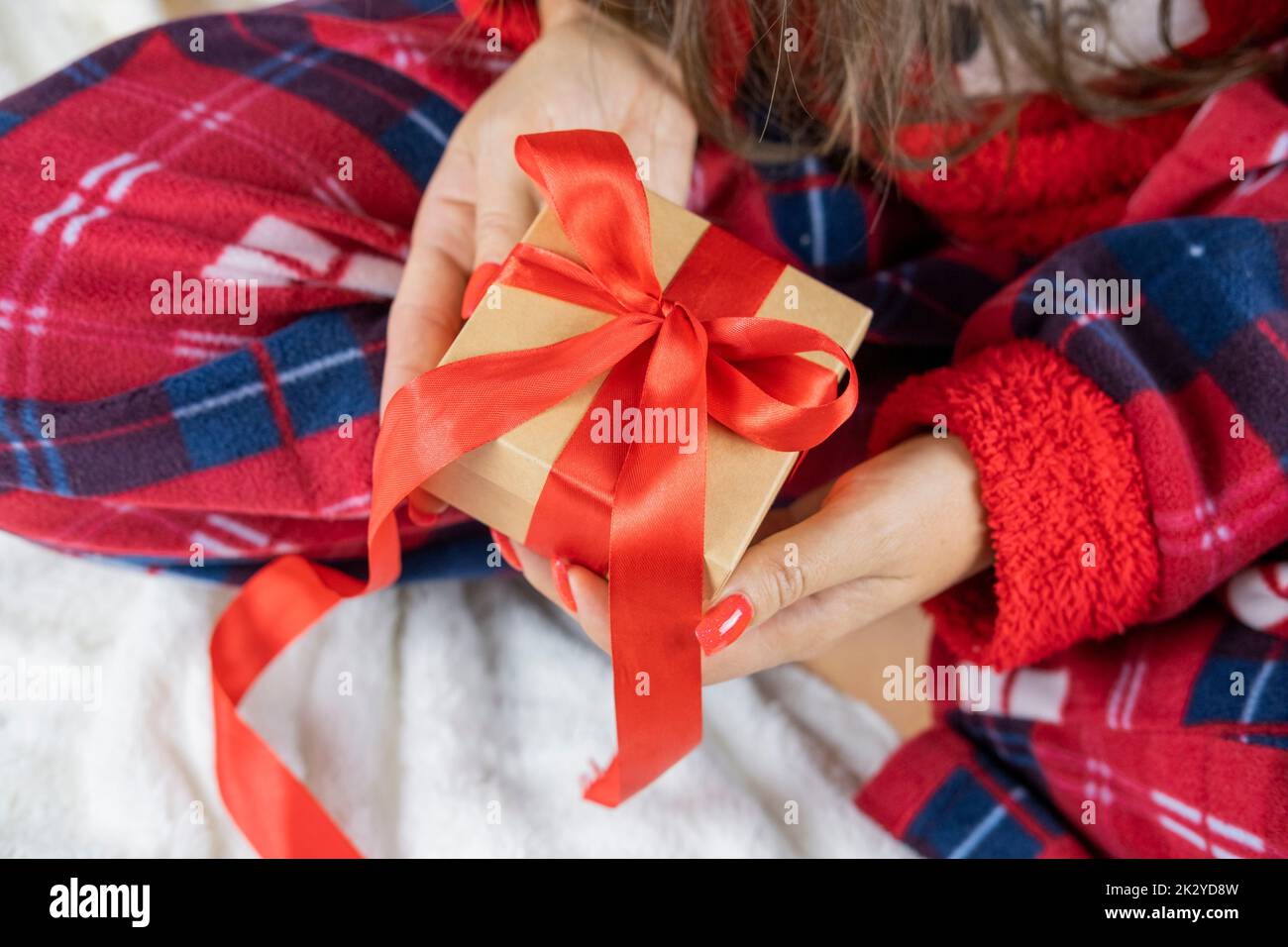 girl in santa claus pajamas holding a box of surprise gift with a red bow for the holiday christmas and new year Stock Photo