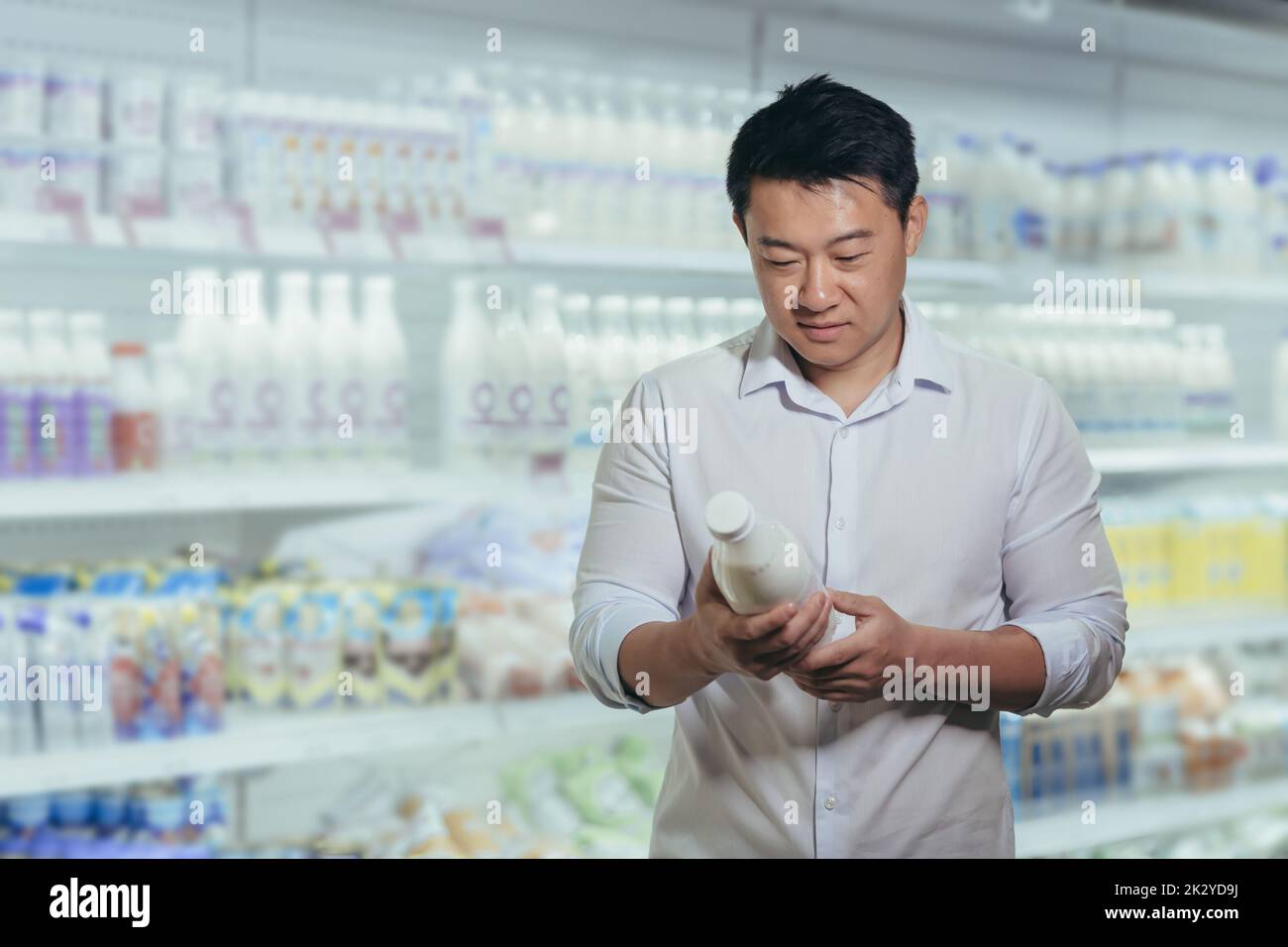 Asian buyer in a supermarket in the dairy department, Man chooses milk reads the label. Stock Photo