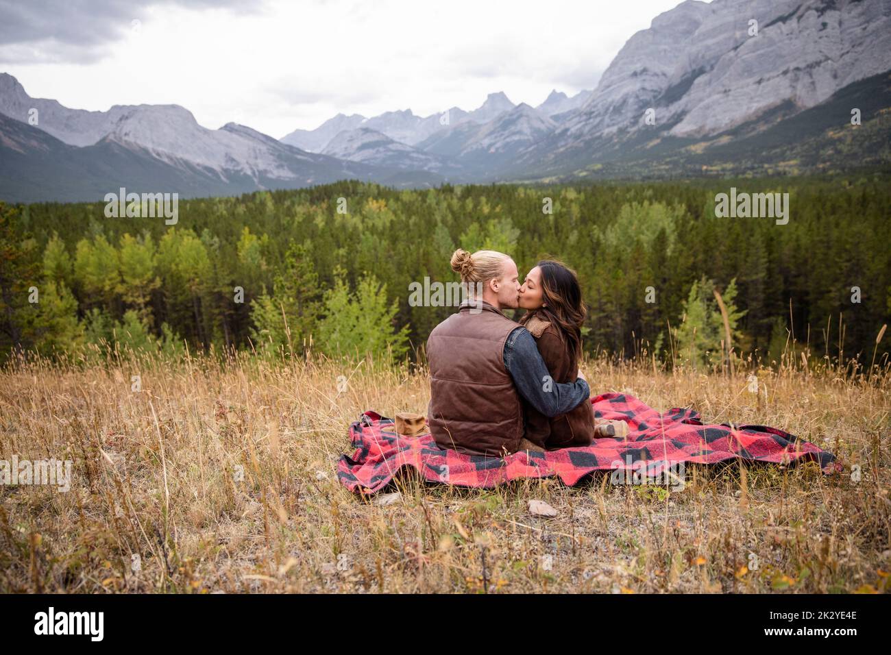 Romantic young couple kissing on blanket on scenic mountain hill Stock