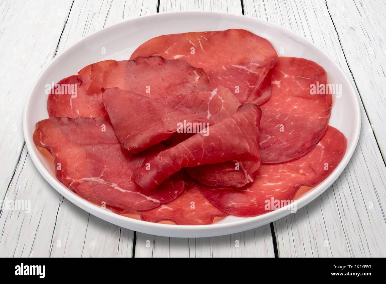 Bresaola slices in plate on white wooden table, italian dried beef salami from Valtellina Stock Photo