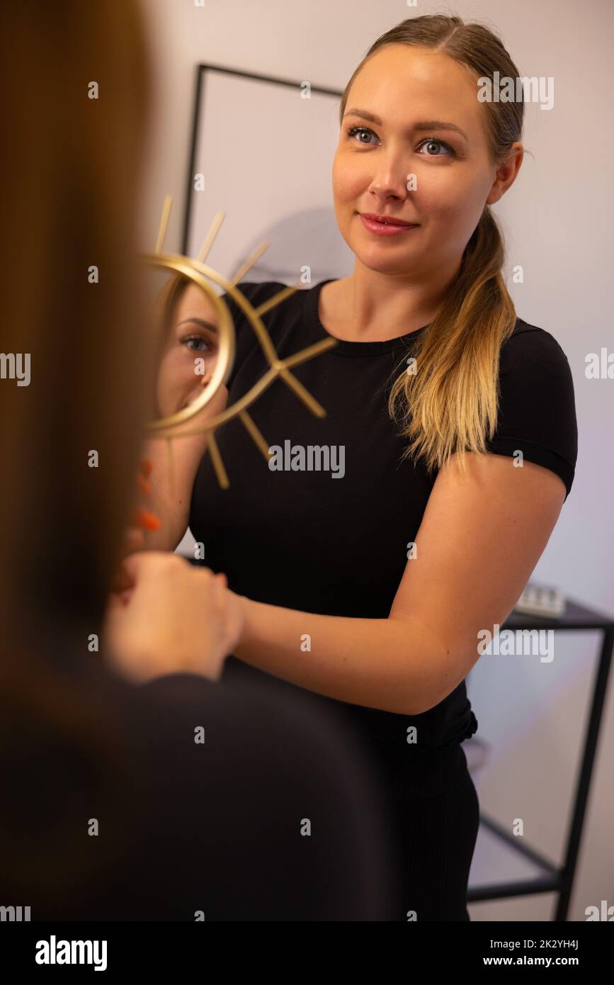 Smiling Beautician Holding Mirror For Female Customer Stock Photo