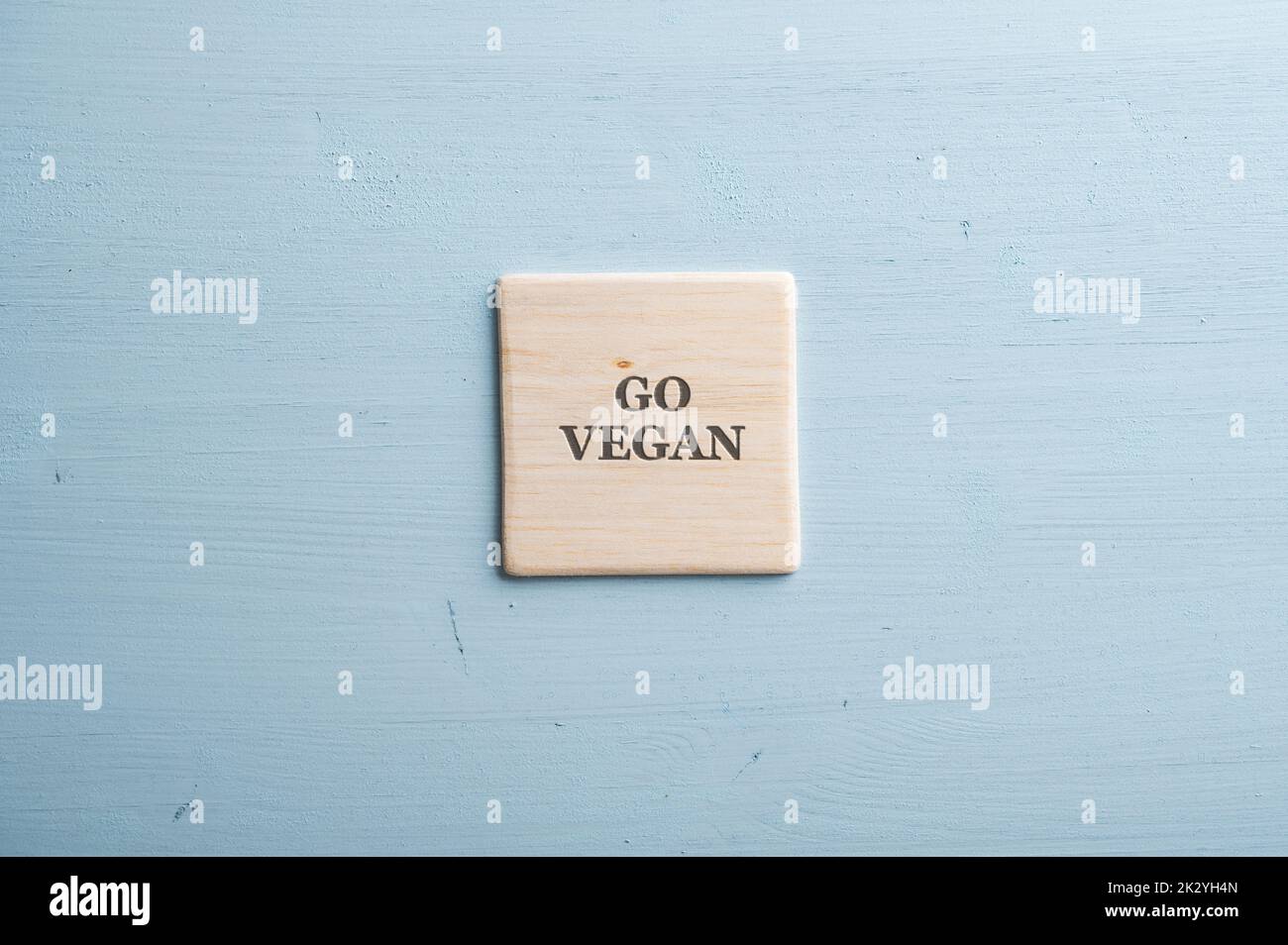 Go vegan sign spelled on wooden tile placed over pastel blue wooden background. Stock Photo