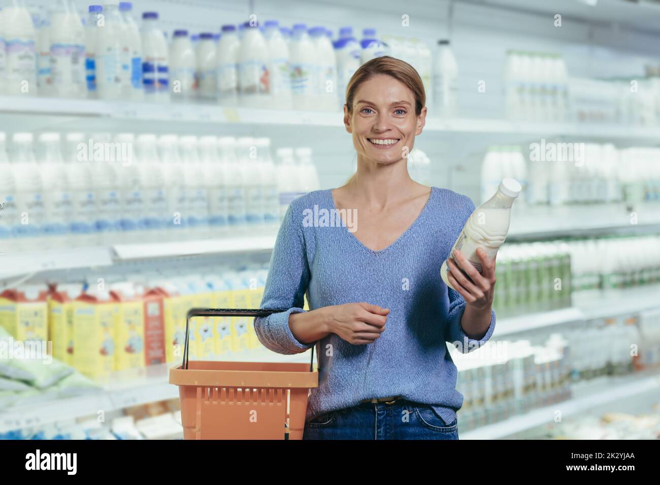 Portrait of a female buyer in a supermarket, a blonde housewife looking at the camera in the dairy department chooses milk and yogurt. Stock Photo