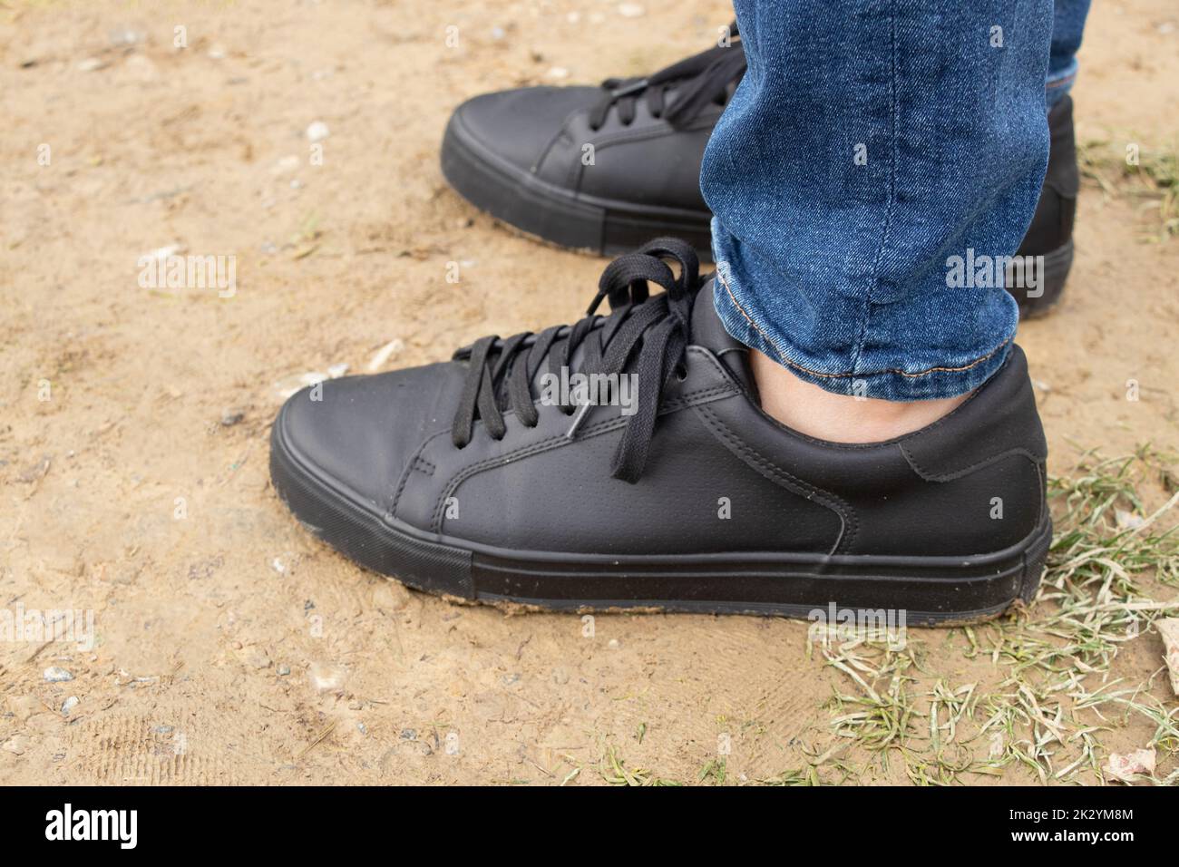 Men's feet in black sneakers and jeans stands on the ground in Ukraine