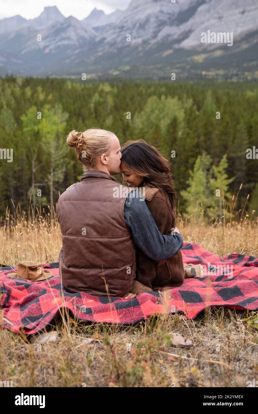Romantic young couple kissing on plaid blanket in mountain woods Stock