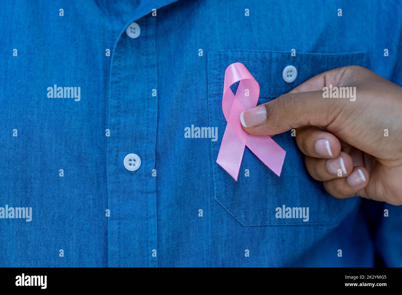 Woman's hand placing pink breast cancer awareness ribbon on a man's chest. Stock Photo