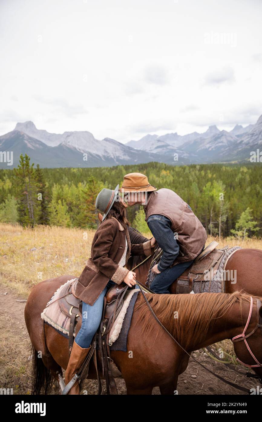 Romantic young couple kissing on horseback on scenic mountain trail Stock Photo