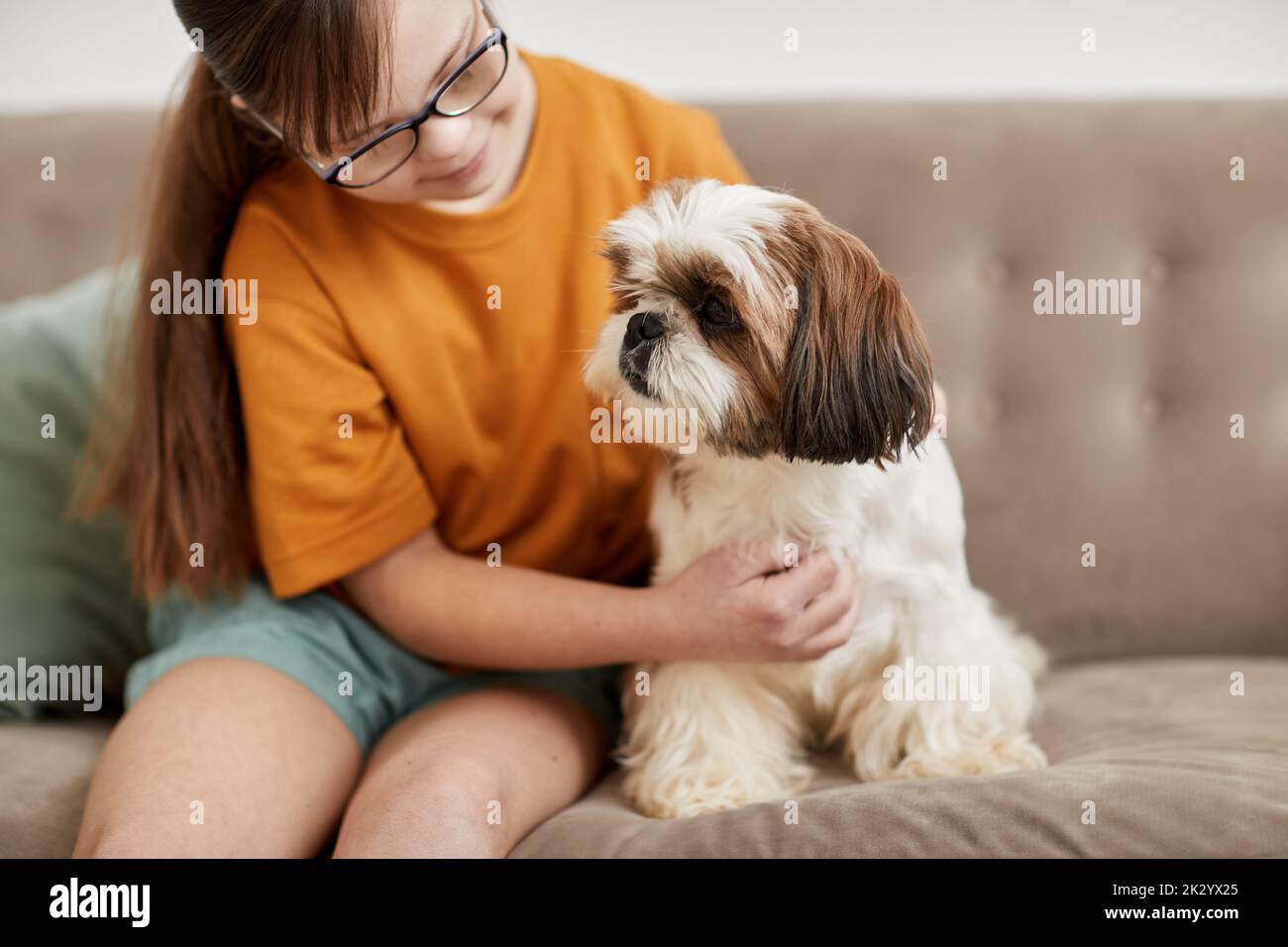 Portrait of cute girl with Down syndrome playing with small dog while sitting on couch together, copy space Stock Photo