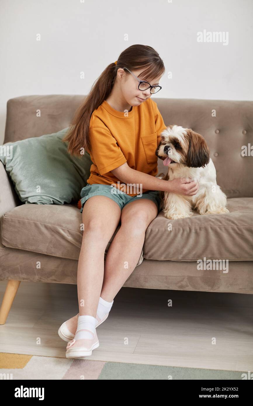 Full length portrait of teenage girl with Down syndrome playing with small dog while sitting on couch together Stock Photo