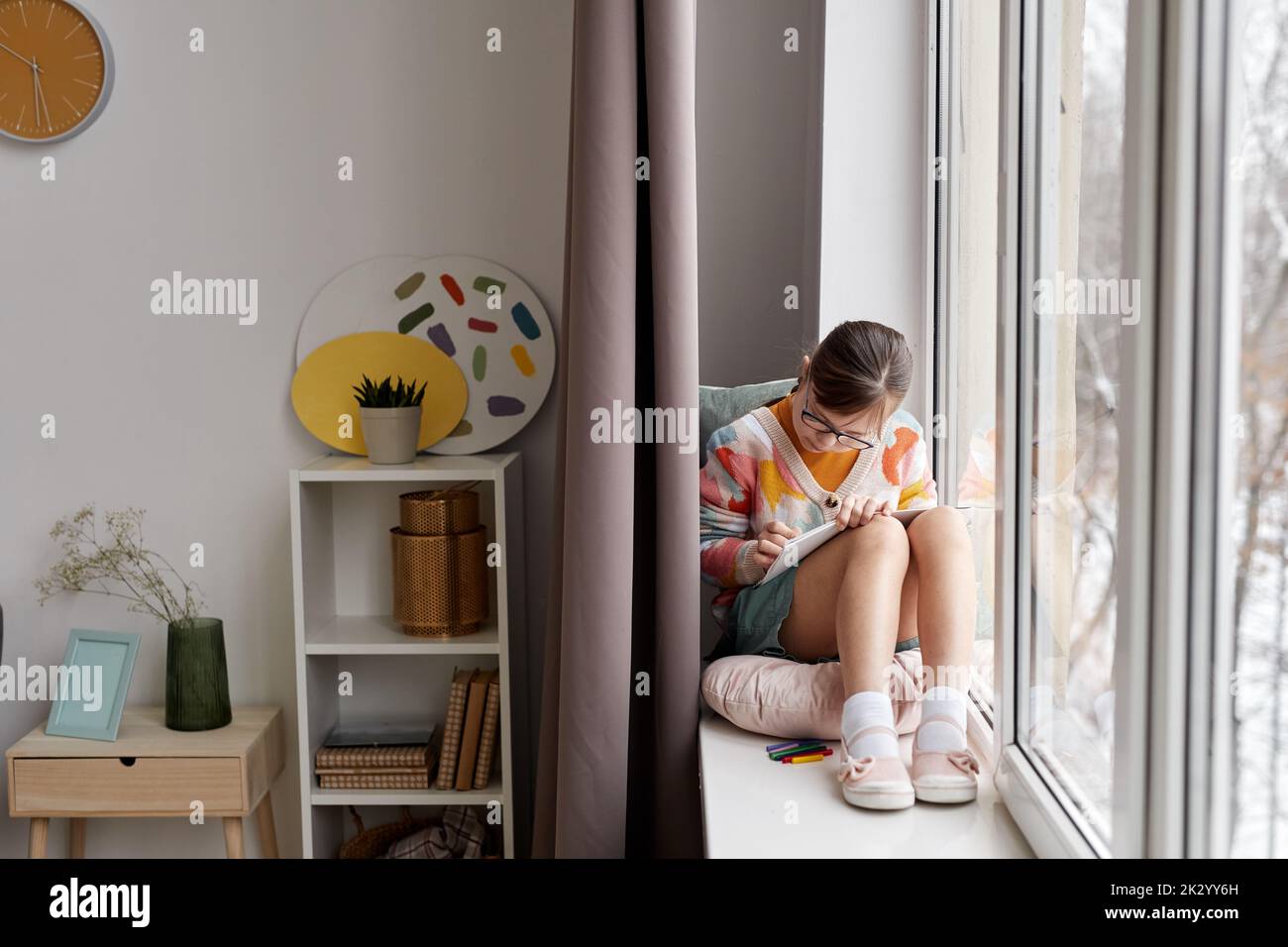Full length portrait of teenage girl drawing pictures while sitting by window in cozy room, copy space Stock Photo