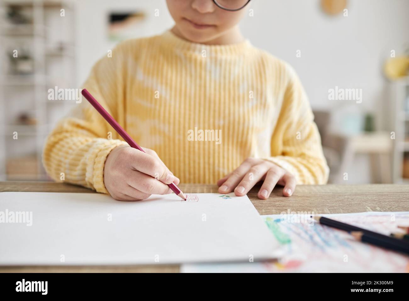 Minimal cropped shot of young girl drawing pictures while sitting at desk at home Stock Photo