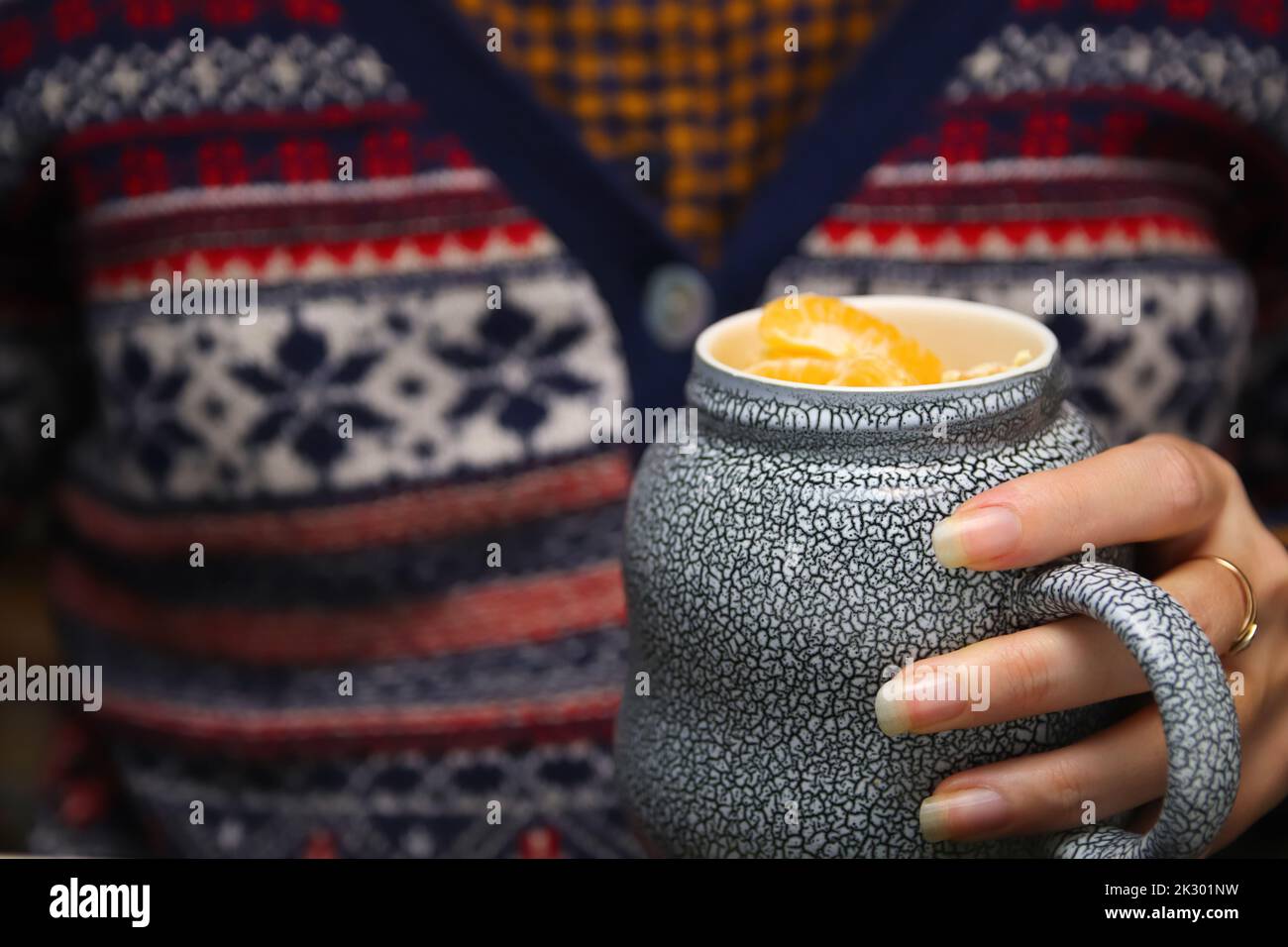 Defocus closeup of female hands with a mug of beverage. Young hipster woman in Christmas sweater holding cup of tea or coffee. Cozy warm ceramic drink Stock Photo