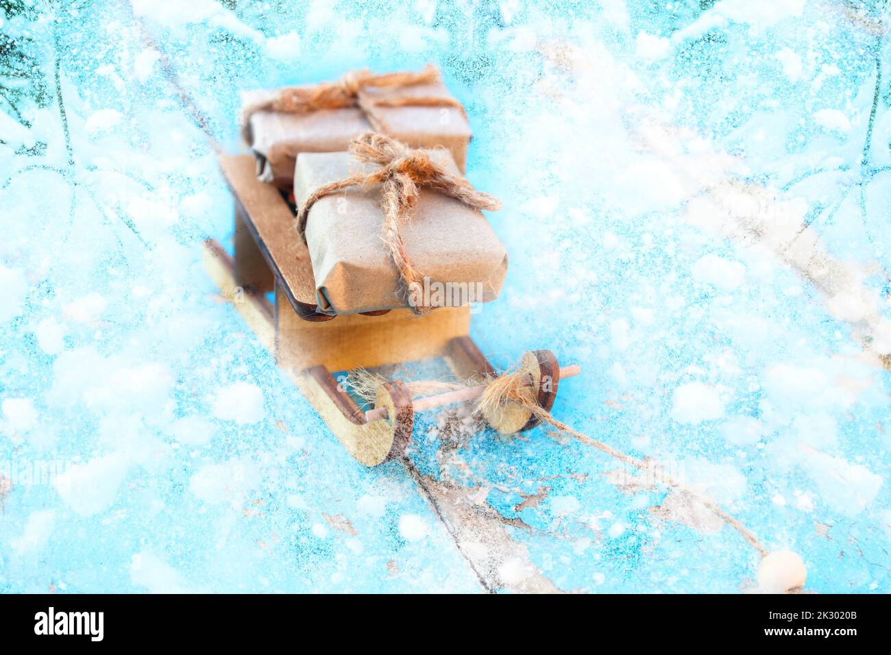 Defocus Xmas gift composition. Wrapped craft vintage gift boxes lying wooden toy sled on blue snowy background. Present box in craft paper. Holiday co Stock Photo
