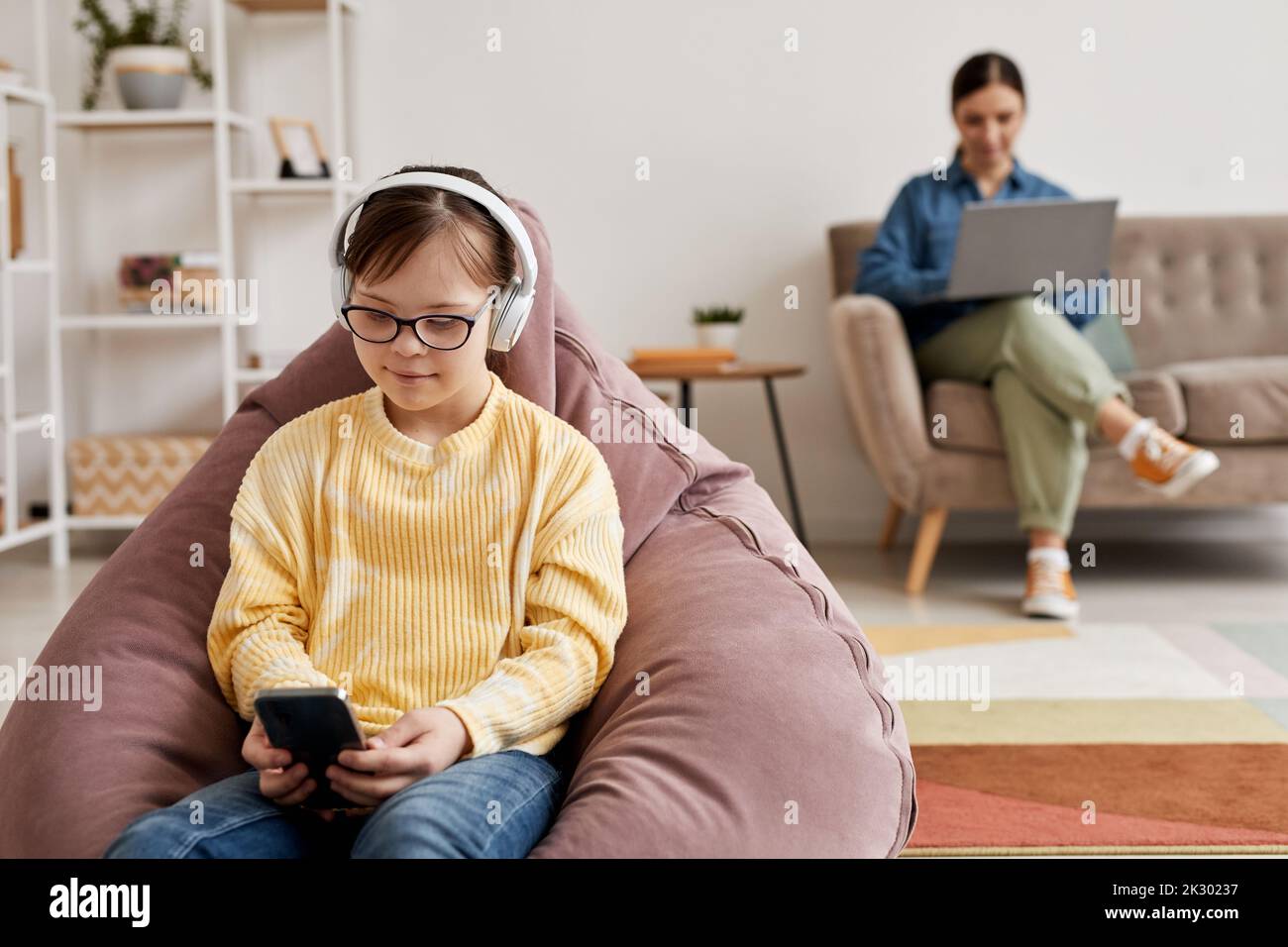 Portrait of teen girl with Down syndrome playing mobile games at home with parent supervision, copy space Stock Photo