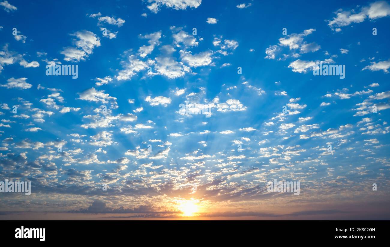 Blue sky with twilight clouds. The sun is setting over the horizon. Yellow dawn. Red sunset. Pink clouds. Stock Photo