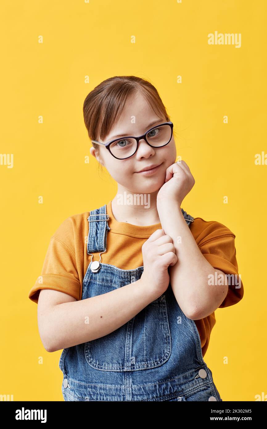 Portrait of teen girl with Down syndrome looking at camera and wearing glasses against yellow background in studio Stock Photo
