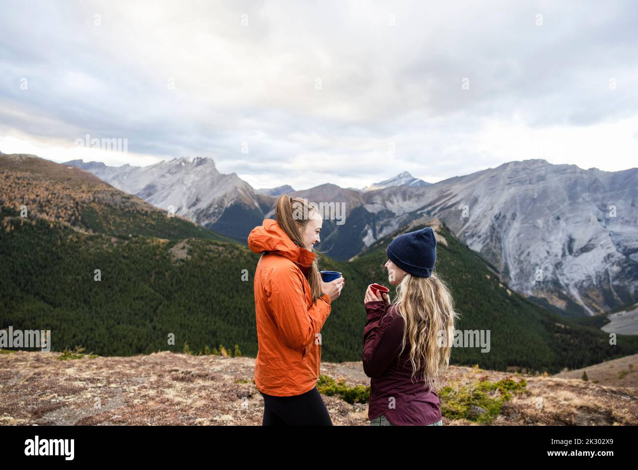 Young women enjoying coffee on majestic mountain summit, Canada Stock Photo
