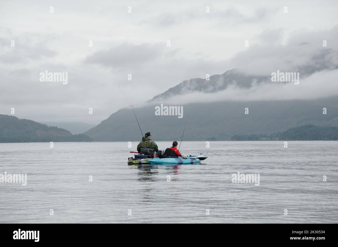 Fishing from kayak on calm water surrounded by mountain scenery Scotland Stock Photo