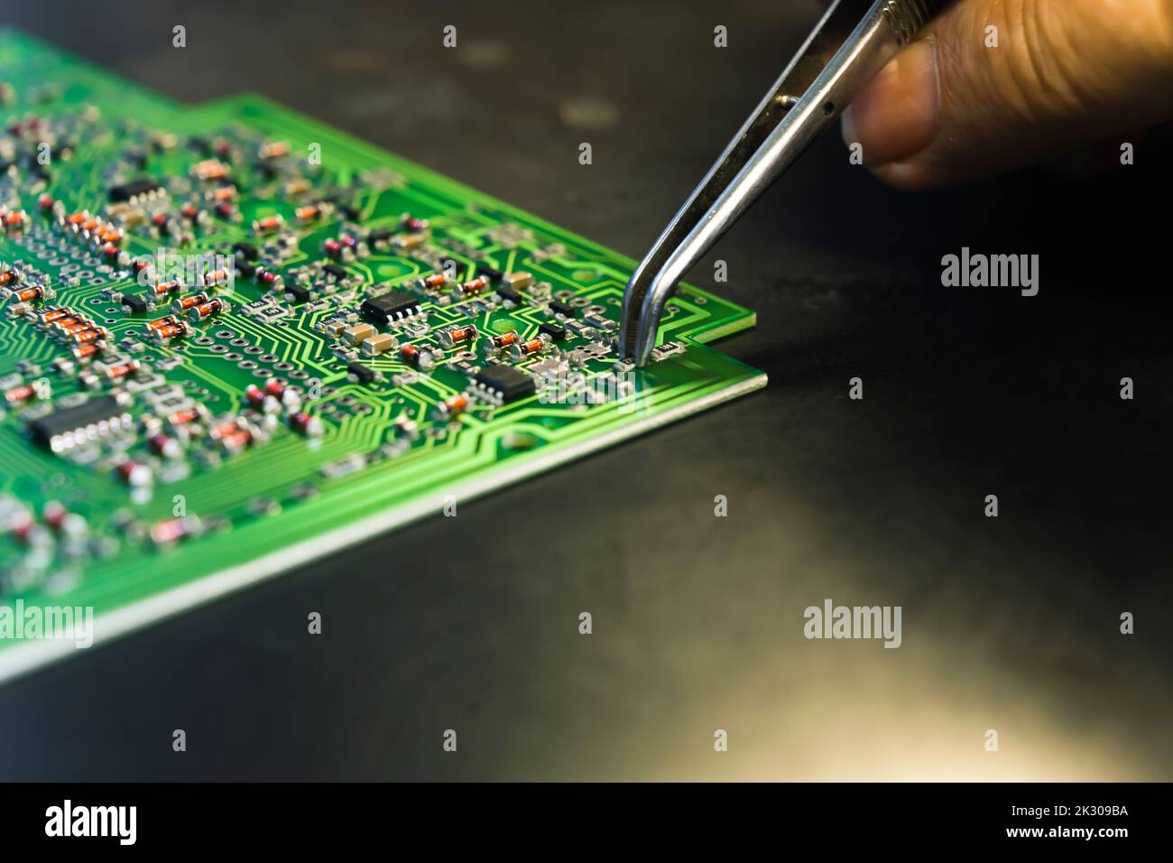 Automatic machines versus human precision. Hand assembly concept. Unrecognizable caucasian hand of a female engineering expert using professional tweezer to slowly place electric components onto PCB. Closeup shot. High quality photo Stock Photo