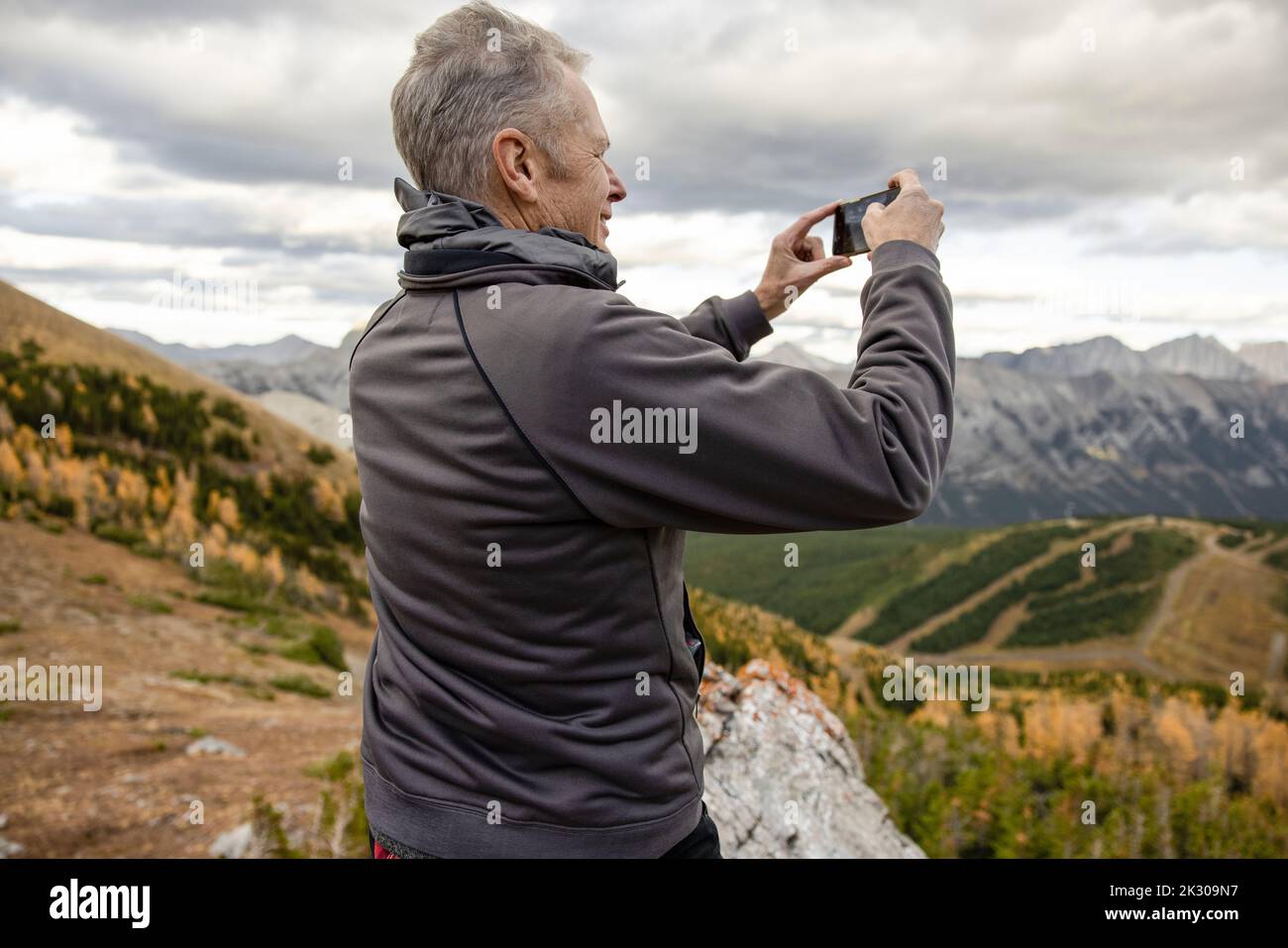 Senior male hiker with camera phone on mountain summit Stock Photo