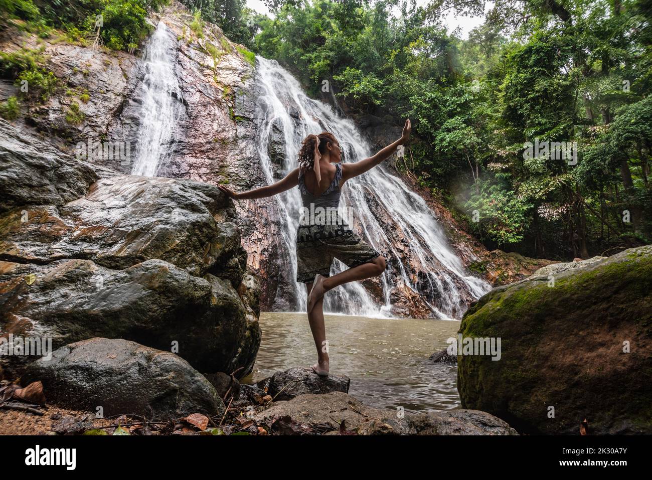 Woman doing yoga posture in front of a waterfall surrounded by ...