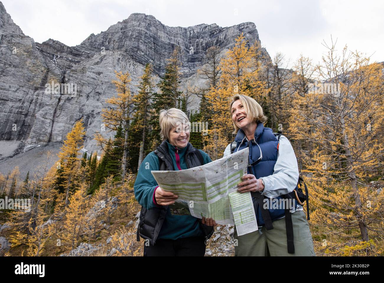 Happy mature female hikers with trail map below autumn mountain Stock