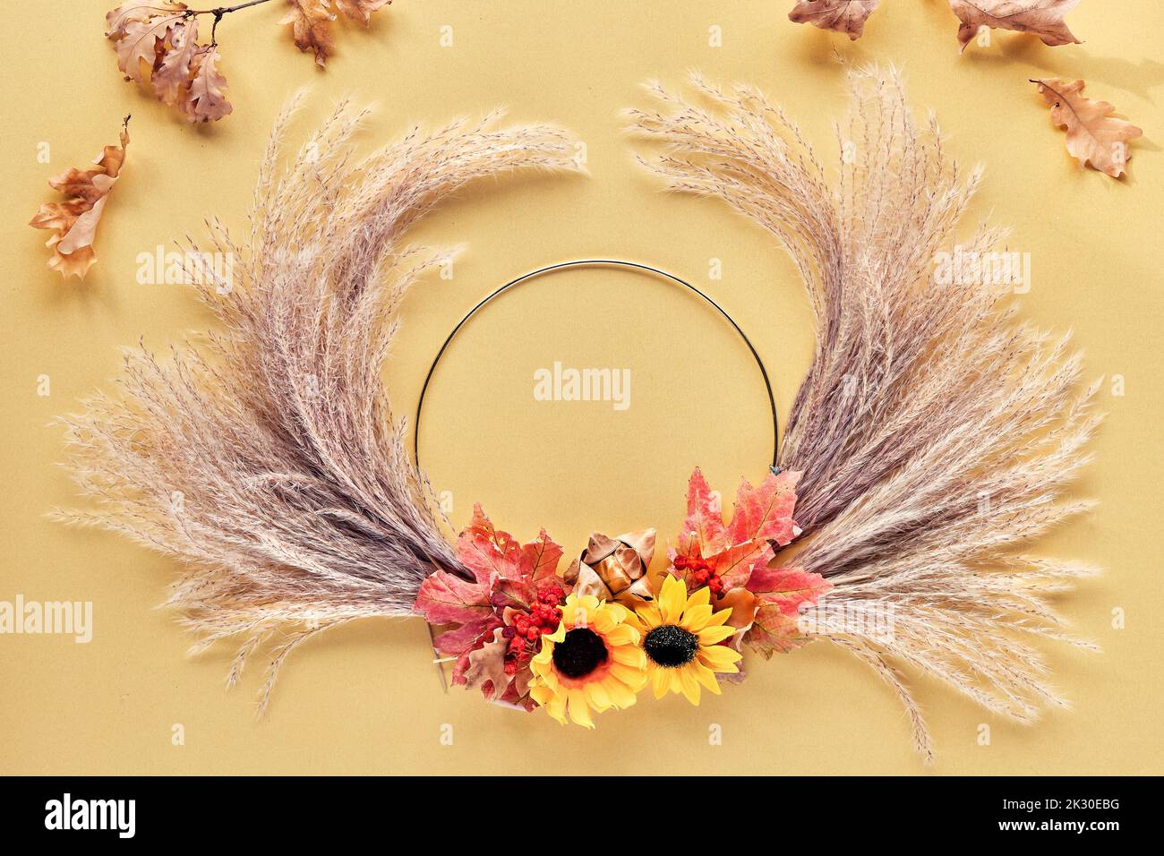 Hands making dried floral wreath from dry pampas grass and Autumn leaves. Flat lay on white yellow table, sunlight with long shadows. Stock Photo