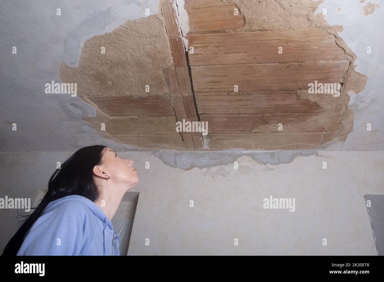 a young woman looking up at a ruined hole in the ceiling. The plaster
