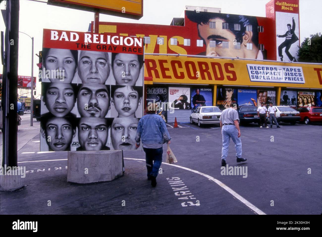 People walking across the parking lot at Tower Records with hand-painted signs of current albums on sale and a large mural of Elvis Presley on the Sunset Strip in Los Angeles, CA Stock Photo